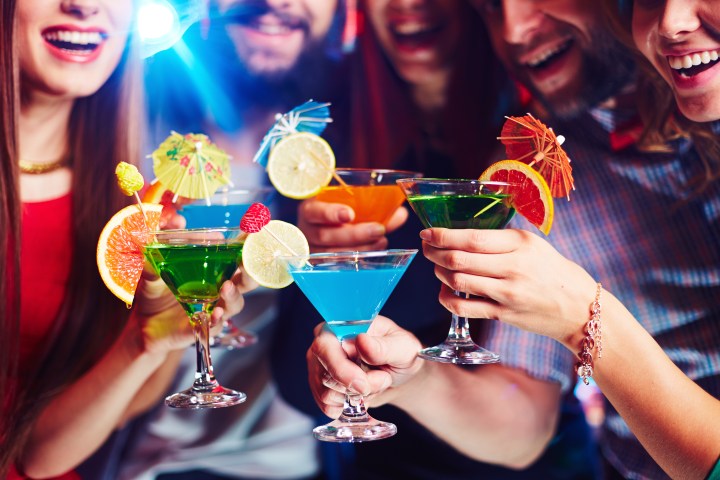 Group of people holding colorful cocktails with garnishes and umbrellas, smiling at a party.